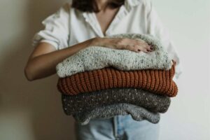 donna che mantiene una serie di maglioni piegati